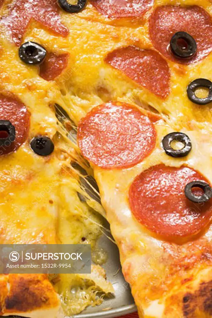 Pizza with salami, cheese and olives, a piece cut (detail)