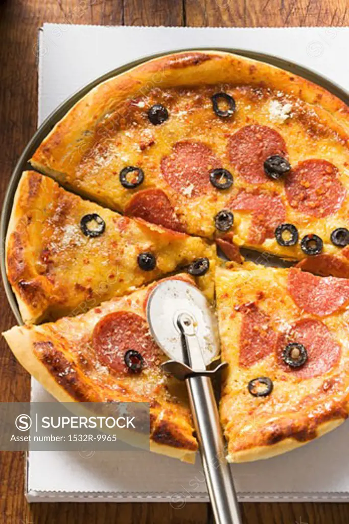 Pizza with salami, cheese and olives with pizza cutter