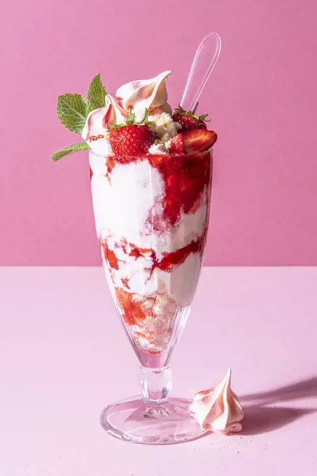 Strawberry sundae with ice cream, whipped cream, crushed meringue, strawberry sauce and mint
