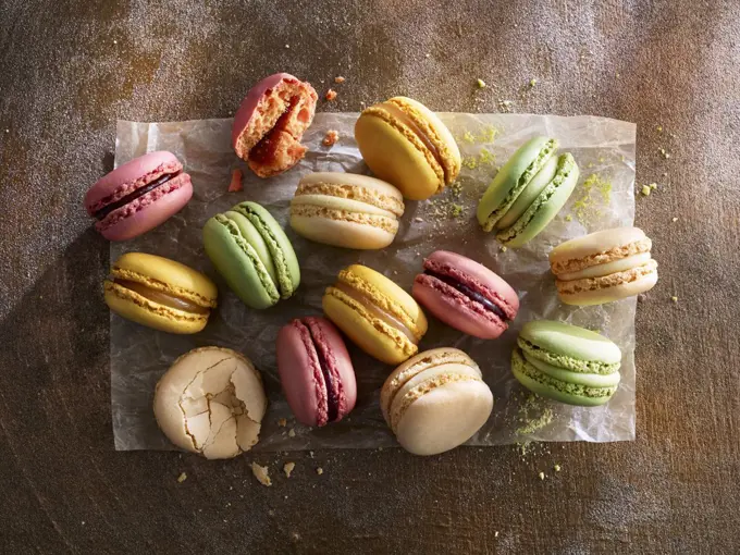 Different colorful macarons on paper against a wooden background