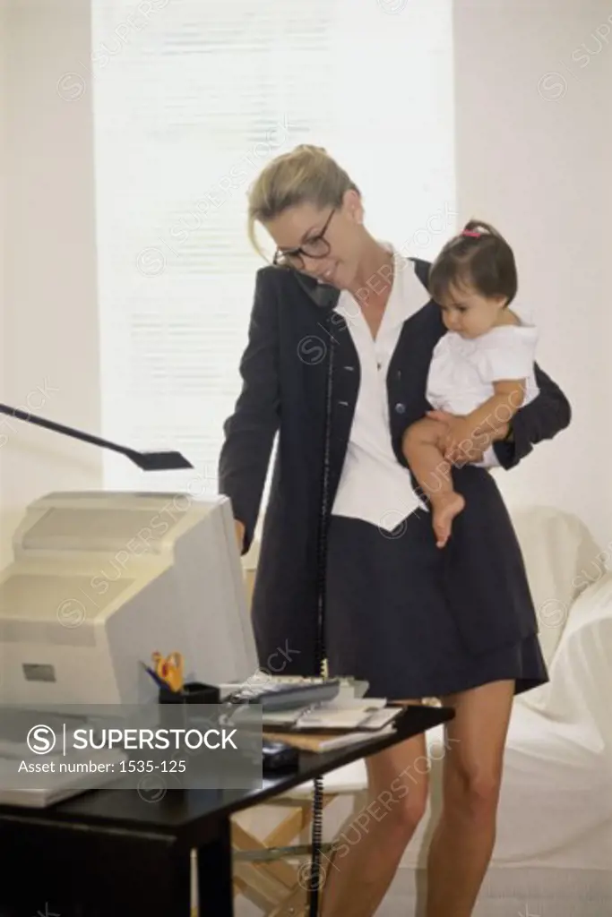 Mother carrying her daughter and talking on the phone in an office