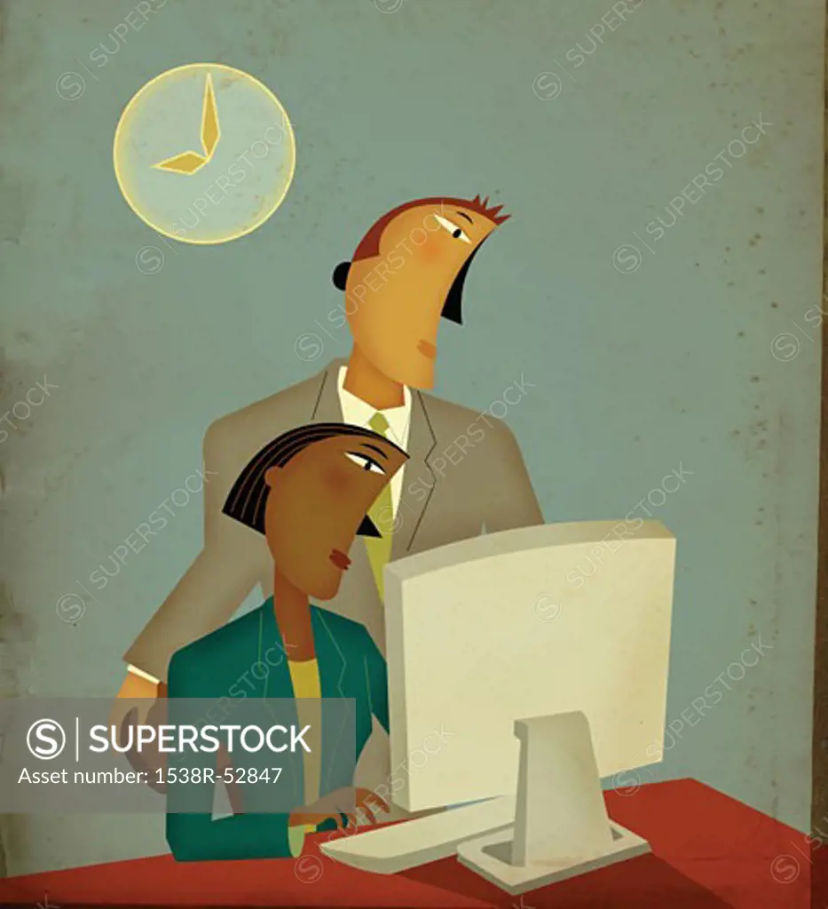 A businessman standing behind a seated woman, both looking at computer screen