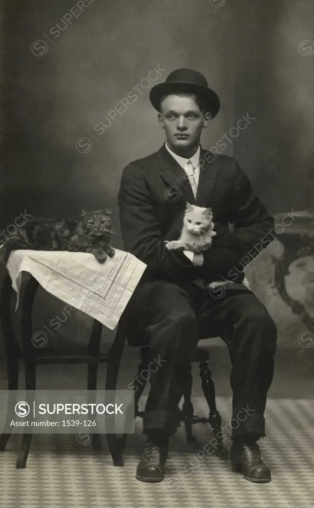 Young man sitting in a chair and holding a kitten, c. 1908