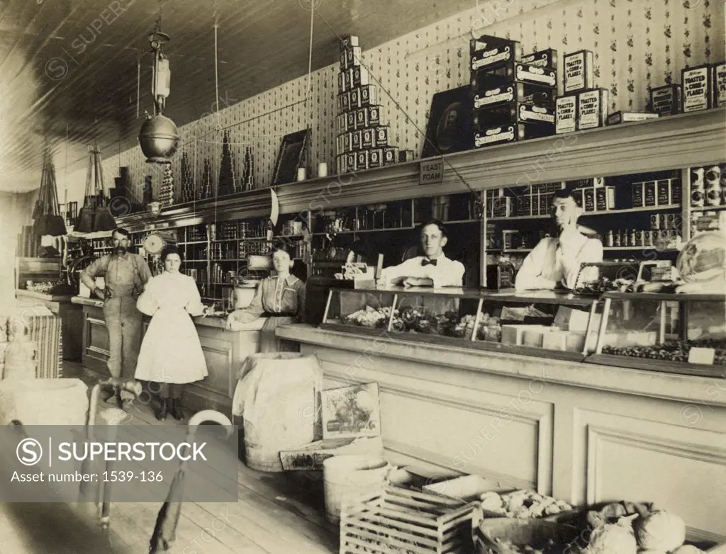 Portrait of three sales clerks and two customers standing in a store, c. 1908