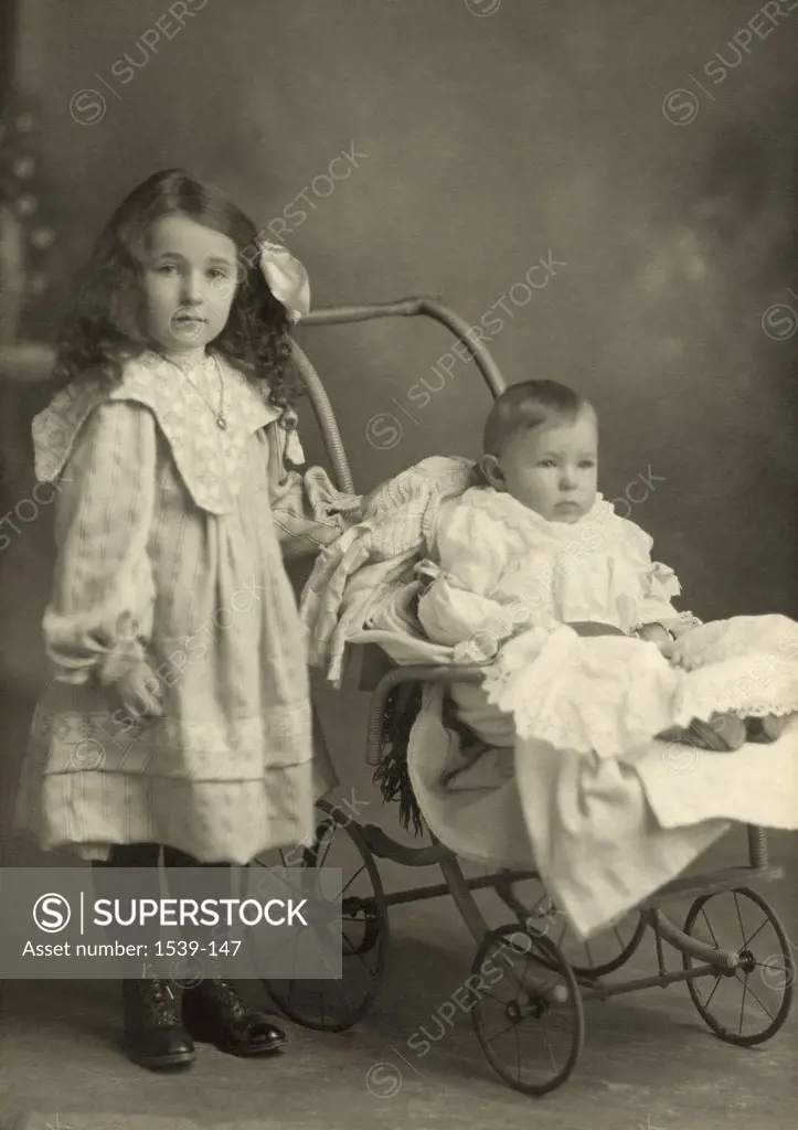 Portrait of a girl standing beside her sister in a baby stroller, c. 1905