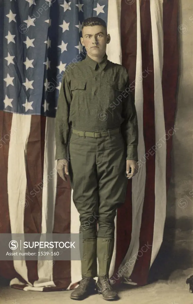 Portrait of an army soldier standing in front of an American flag, c. 1918