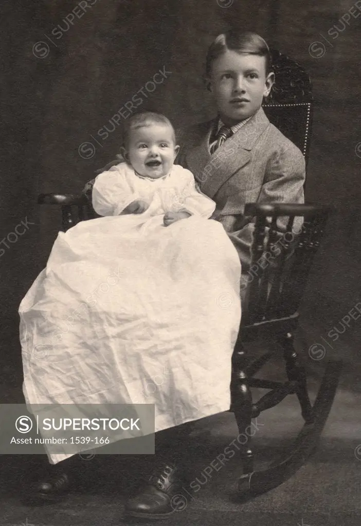 Boy sitting with his sister in a rocking chair, c. 1915