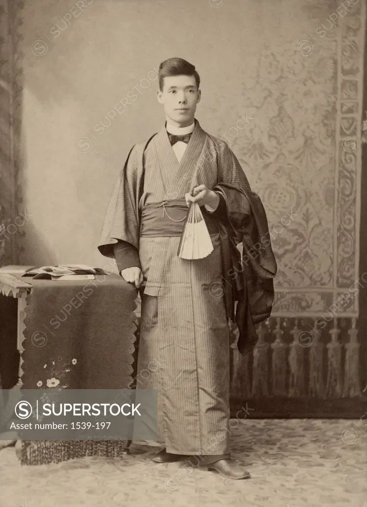 Young man wearing traditional clothing holding a fan, 1900