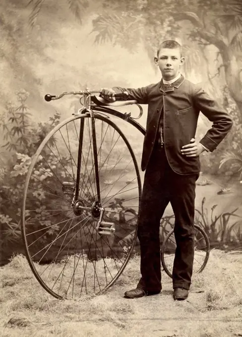 Young man in suit posing with penny farthing, high wheel bicycle, ca. 1885