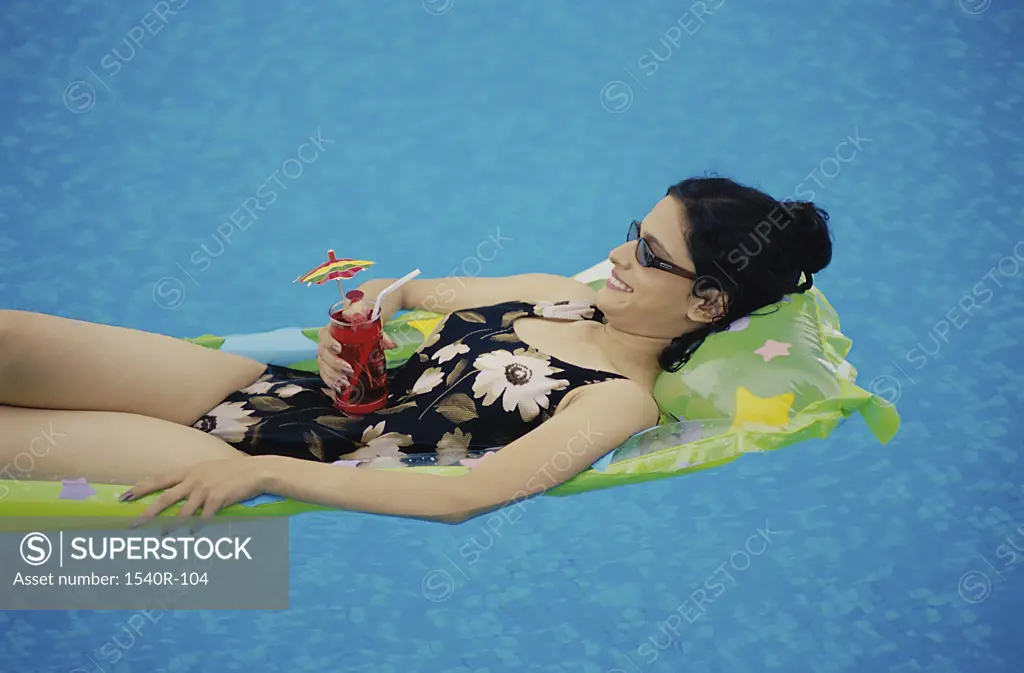 Side profile of a young woman lying on a pool raft holding a drink