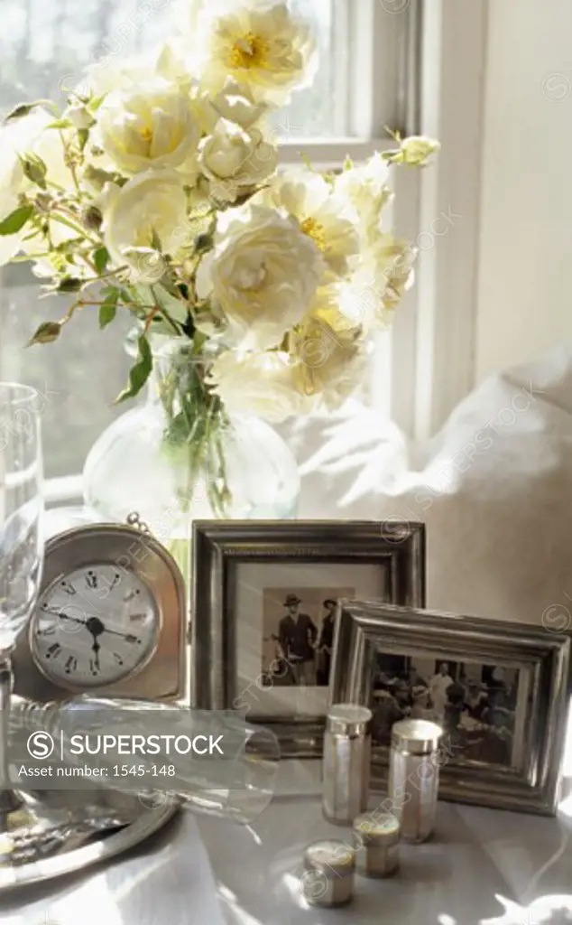 Close-up of picture frames with a flower vase and a clock near a window