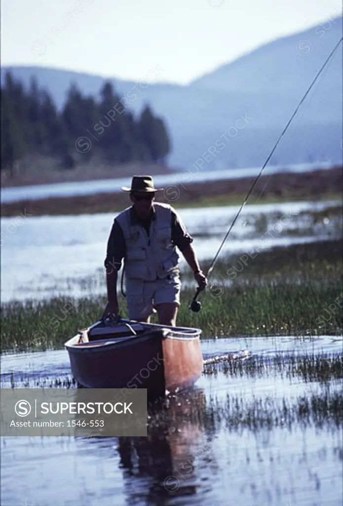 Man walking near a rowboat and holding a fishing rod