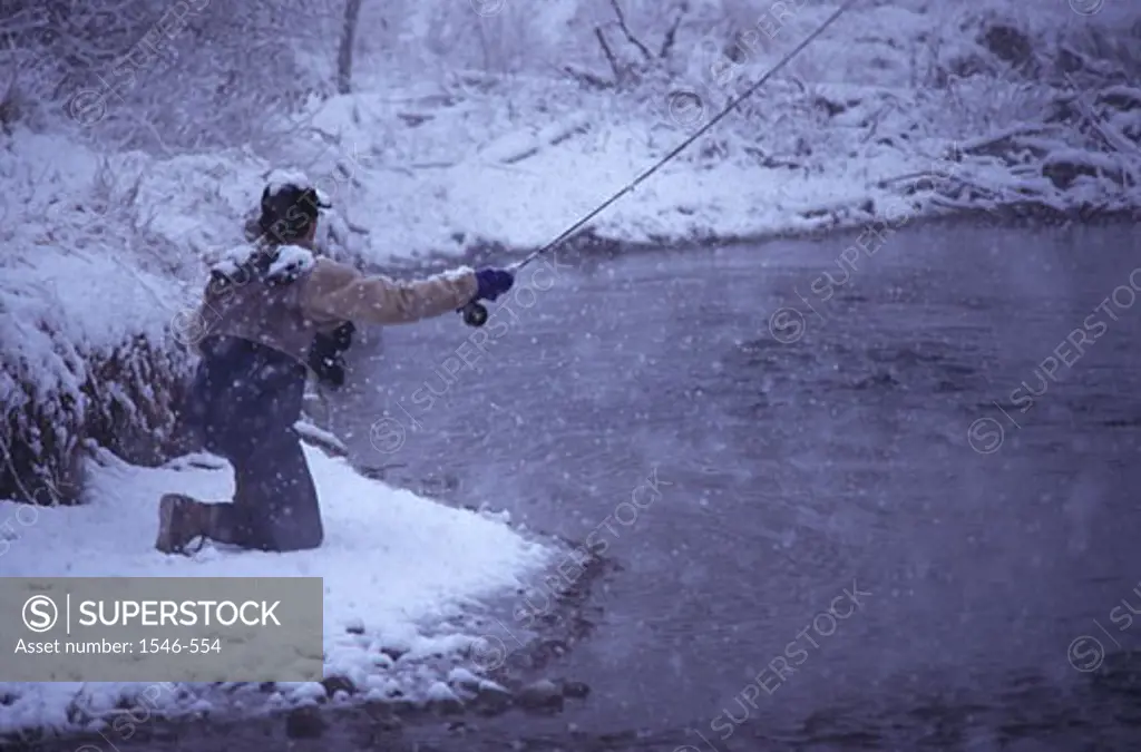 Man kneeling on snow and fly-fishing