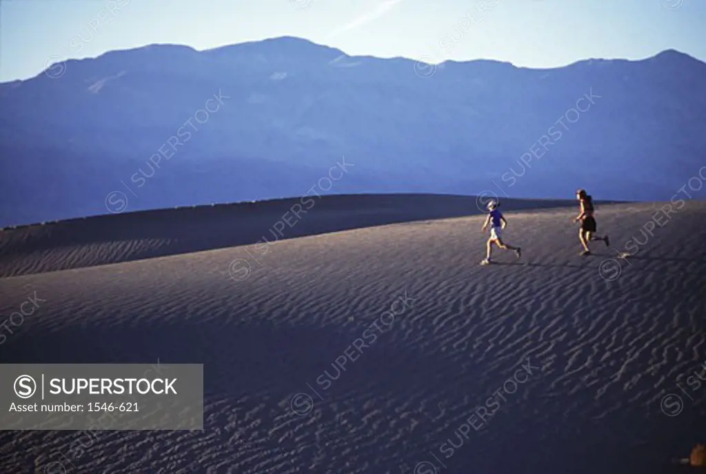 Two people running down a sand dune