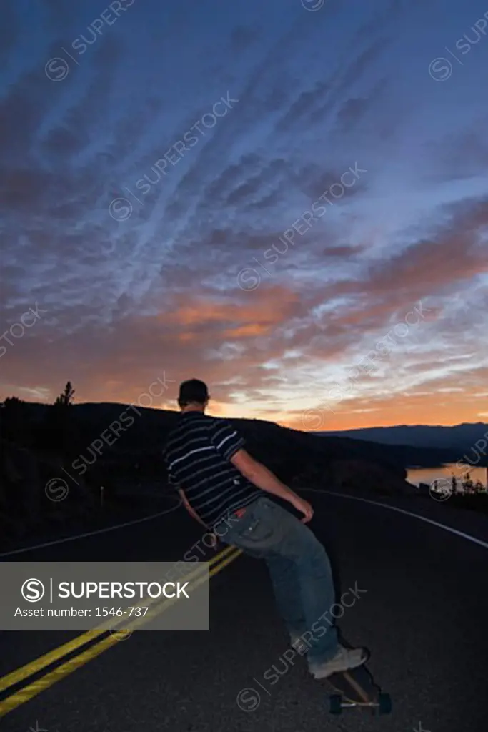 Rear view of a man skateboarding on the road at dawn, Donner Summit, California, USA