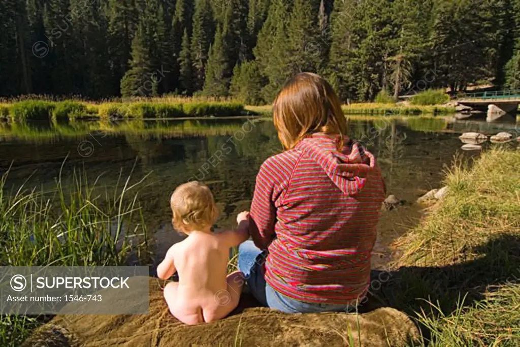 Rear view of a woman sitting on the riverbank with her daughter, Truckee River, California, USA