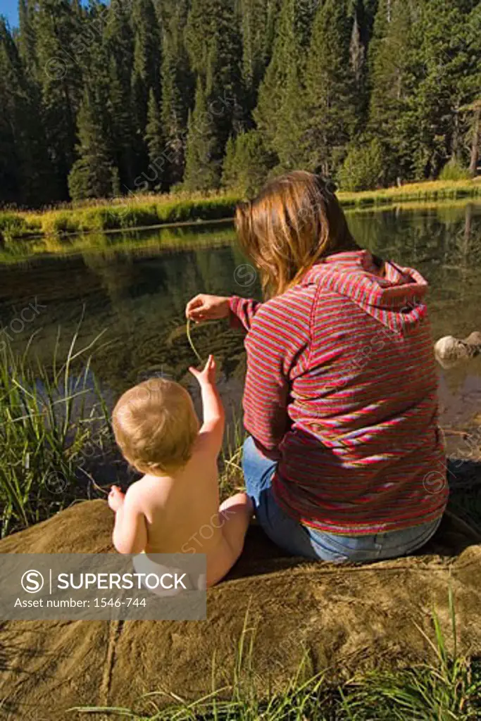 Rear view of a woman sitting on the riverbank with her daughter, Truckee River, California, USA