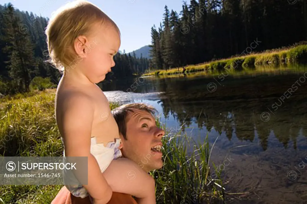 Young man carrying his daughter on his shoulders, Truckee River, California, USA
