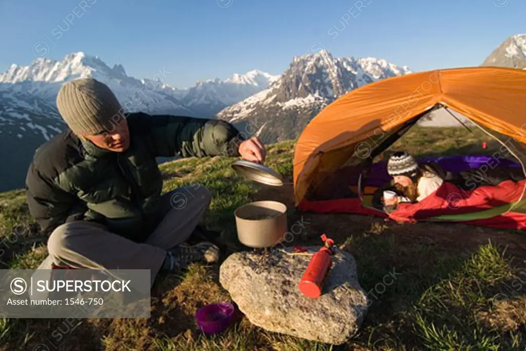 Mid adult man preparing food during camping and a mid adult woman resting in a tent, Aiguilles Rouges, Chamonix, France