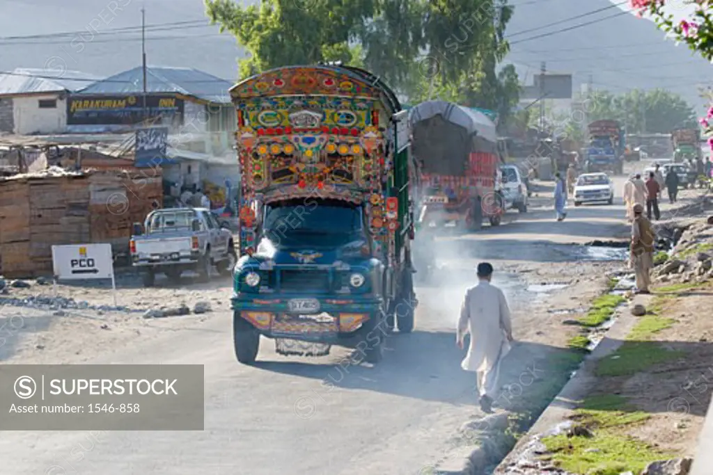 Ornate trucks cars and pedestrians on the main street of a town, Karakoram Highway, Pakistan