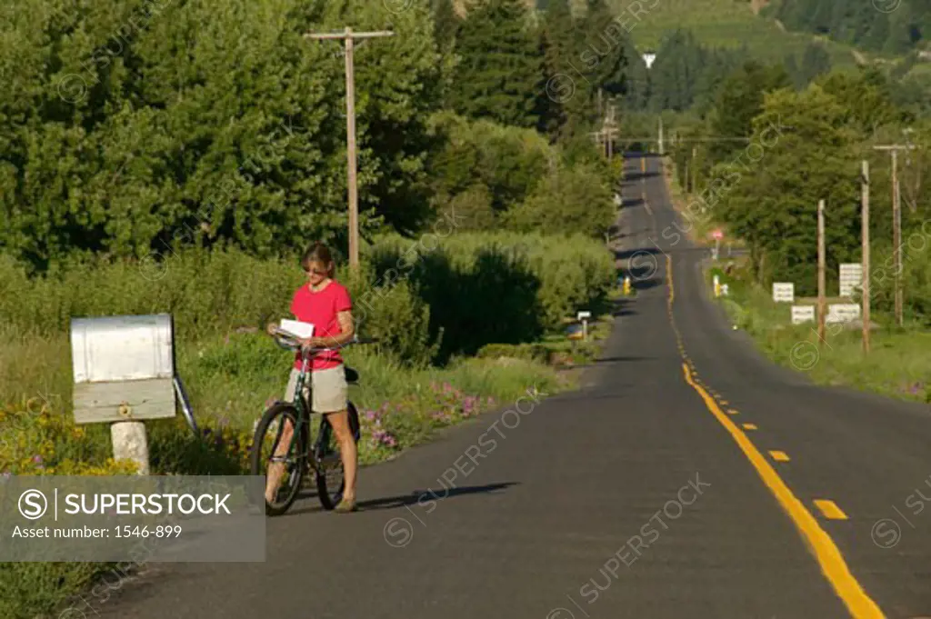 Woman reading a mail by a country mailbox while riding a bicycle, Parkdale, Hood River County, Oregon, USA