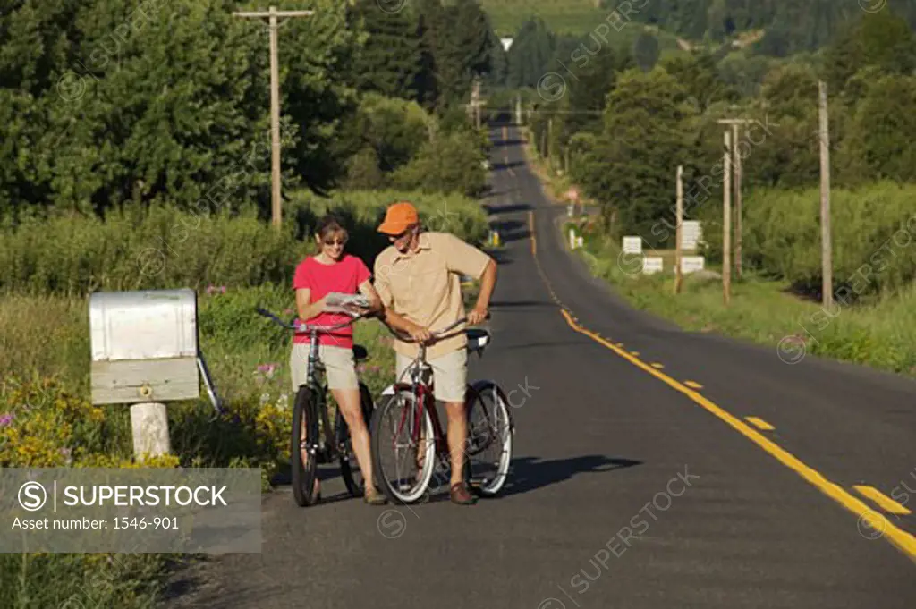 Couple reading mails by a mailbox while riding bicycles, Parkdale, Hood River County, Oregon, USA