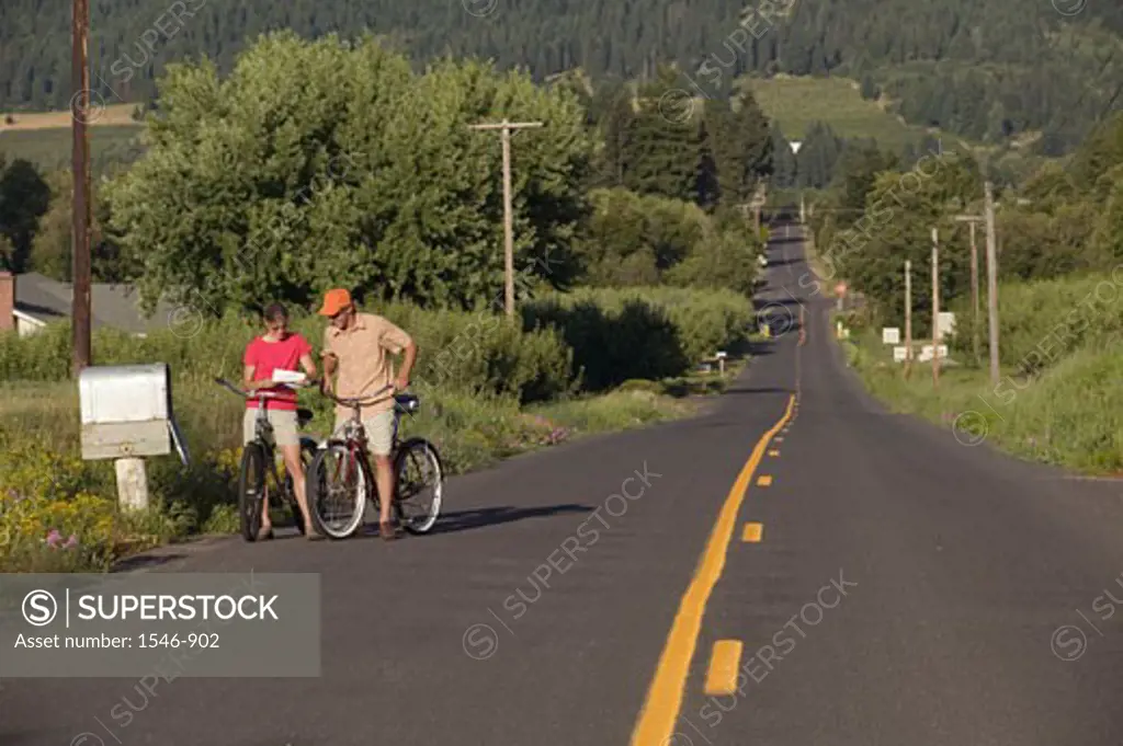 Couple reading mails by a mailbox while riding bicycles, Parkdale, Hood River County, Oregon, USA