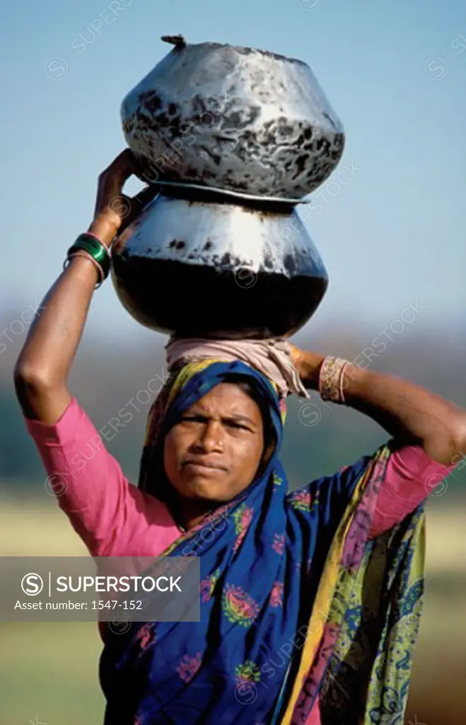 Portrait of a mid adult woman carrying vessels on her head, India