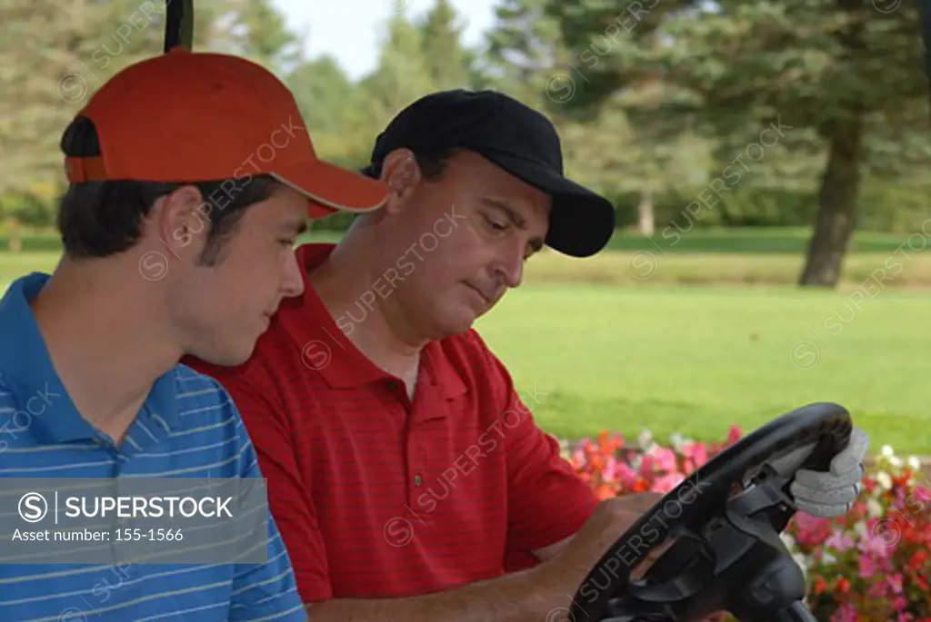 Mature man and his son updating scorecard in a golf cart