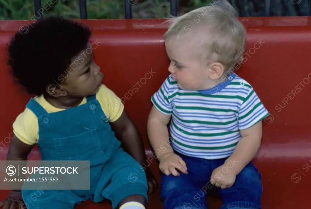 Close-up of two baby boys sitting on a park bench