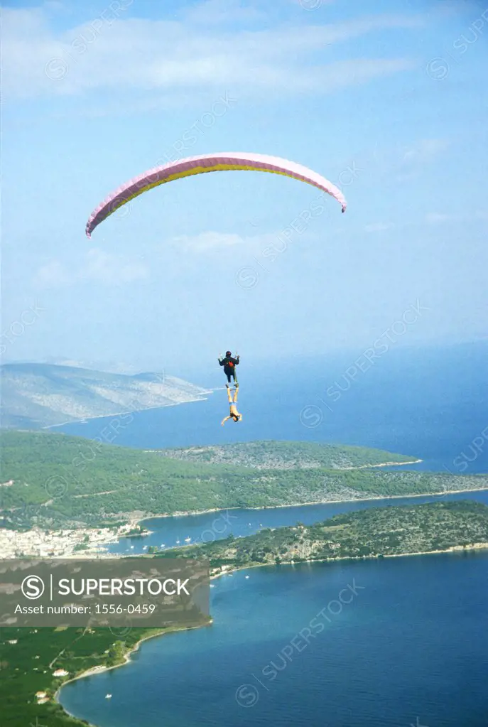 Trapeze artist performing underneath tandem paraglider, Epidauros, Pelopponese Mountains