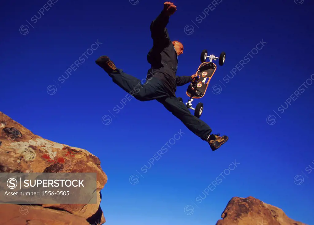 Young adult man jumping from rock to rock holding mountain board