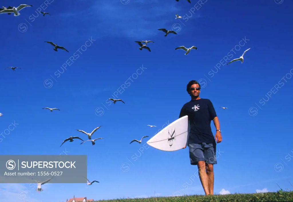 Young man strolling outdoors carrying surfboard