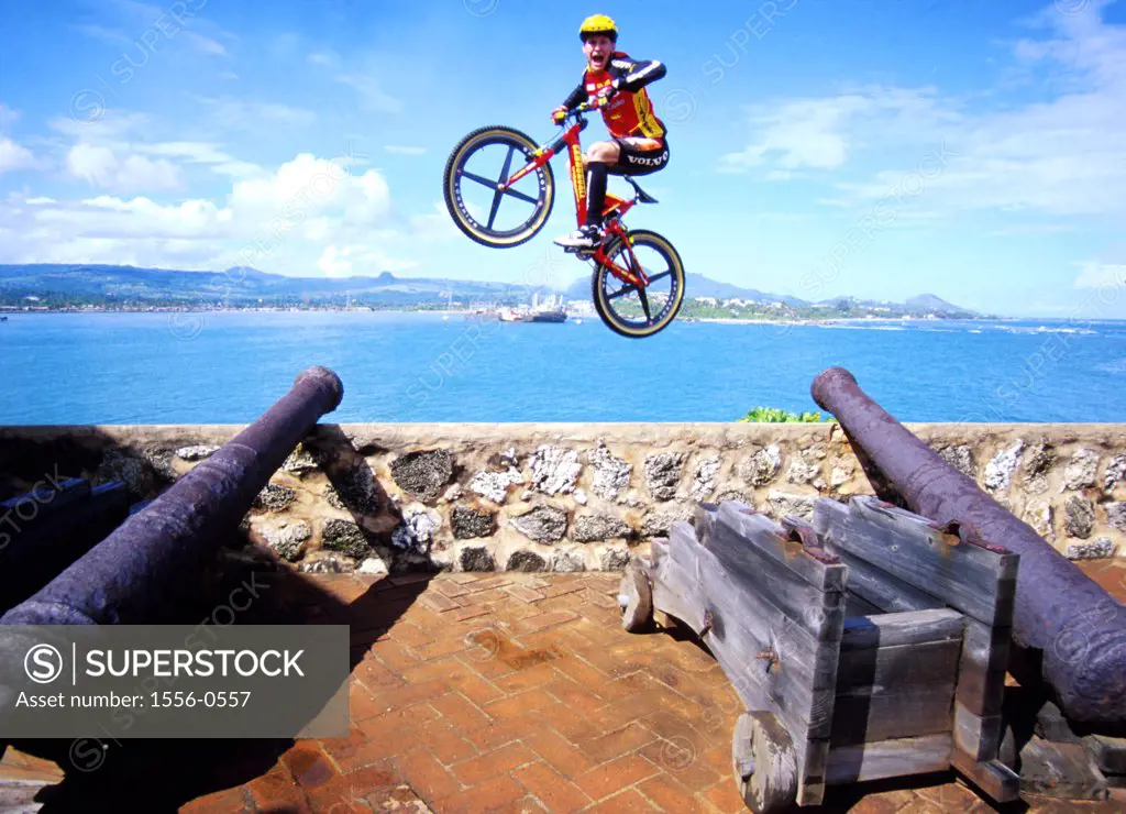 Young adult man jumping over cannons on mountain bike