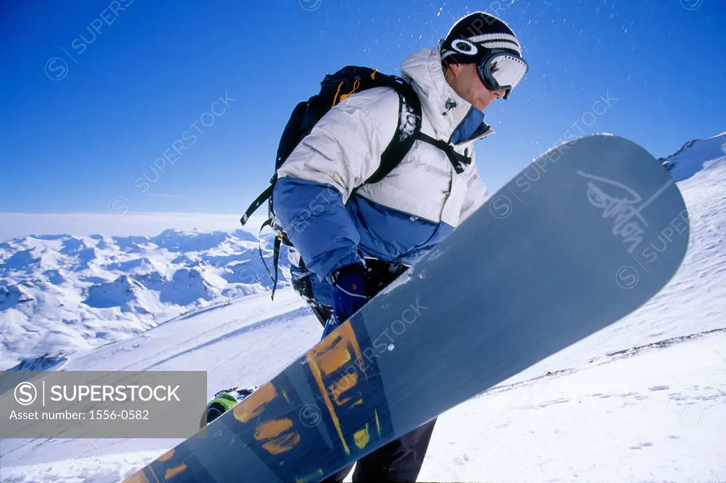 Young adult man carrying snowboard uphill, Tignes, France
