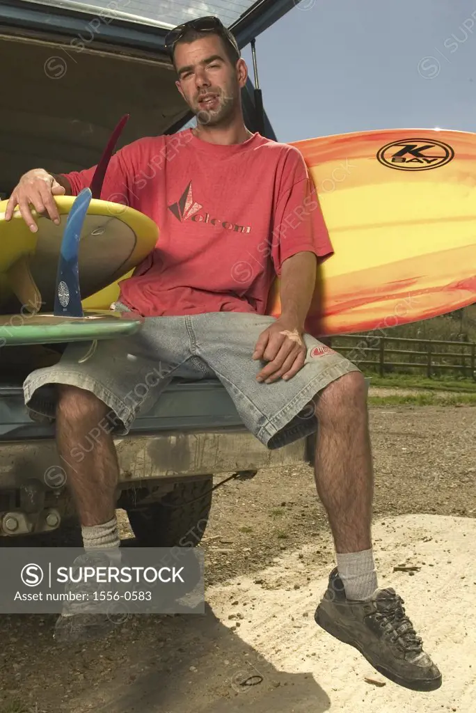 Young adult man sitting with surfboards