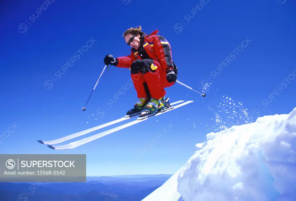 Young adult man jumping while skiing downhill