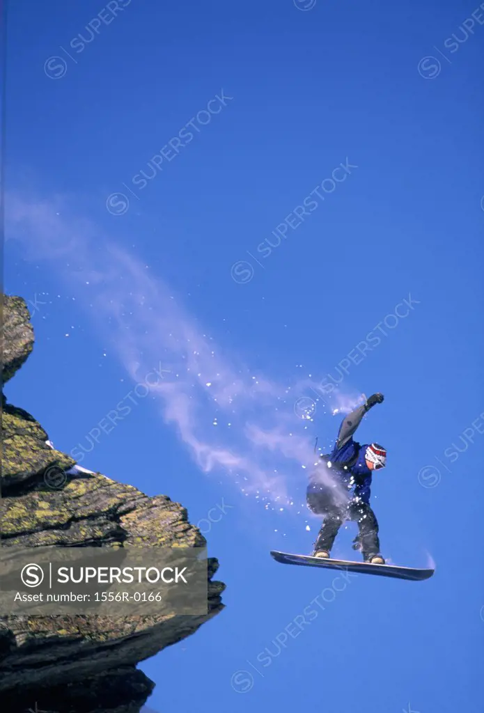 Teenager jumping off cliff on snowboard