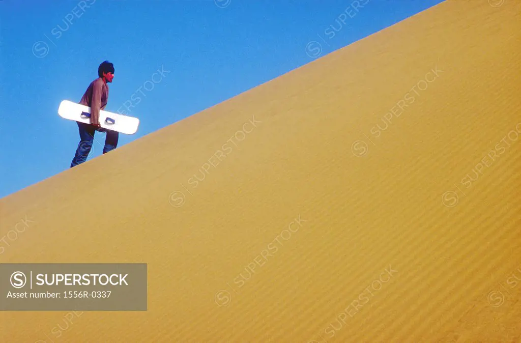 Young adult man carrying sandboard uphill, Peru