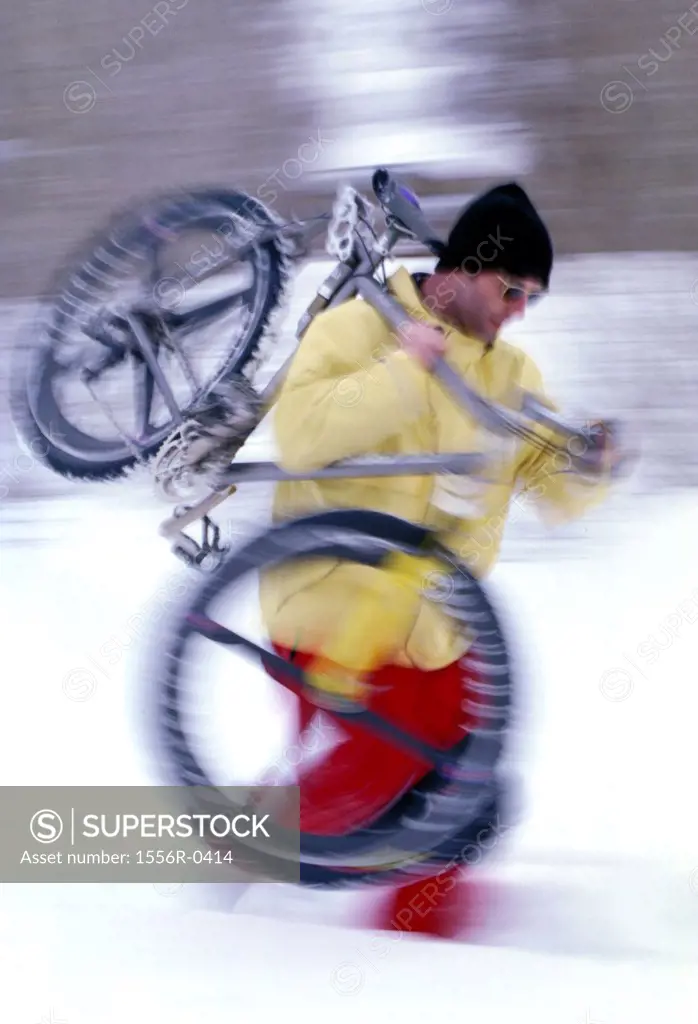 Young man carrying bicycle through snow