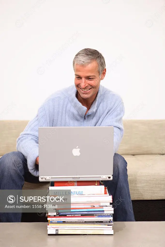 Man, smiles, laptop, data input, Bücherstapel, sofa, sits, no property release, series, people 40-50 years grey-haired, leisure time, Lifestyle, hobby...