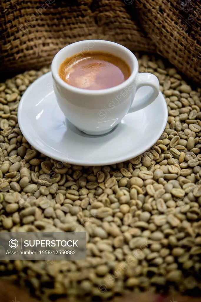 Cup of espresso on a sack with unroasted coffee beans