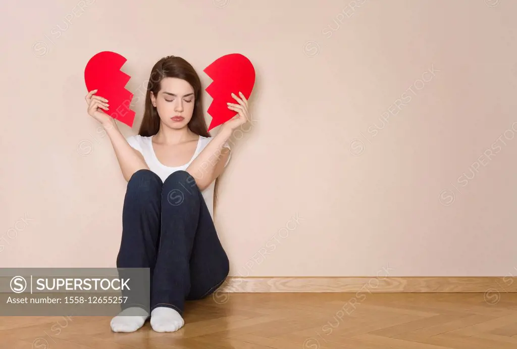 Woman holds divided heart in her hands, sits sadly on the floor,