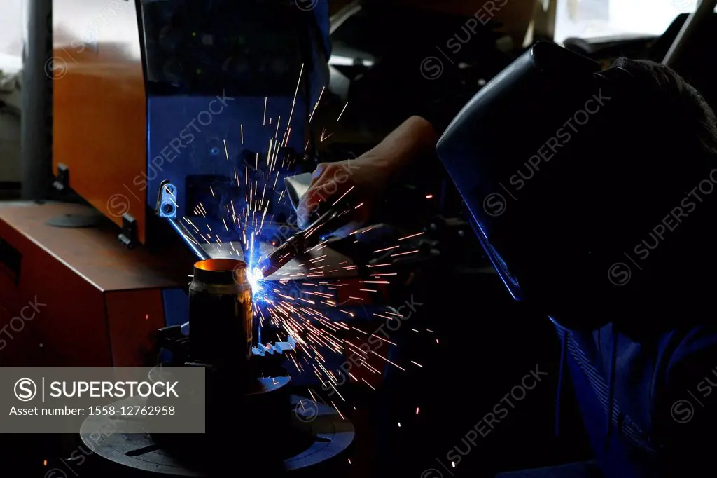 Man welding workpiece, workshop, flying sparks