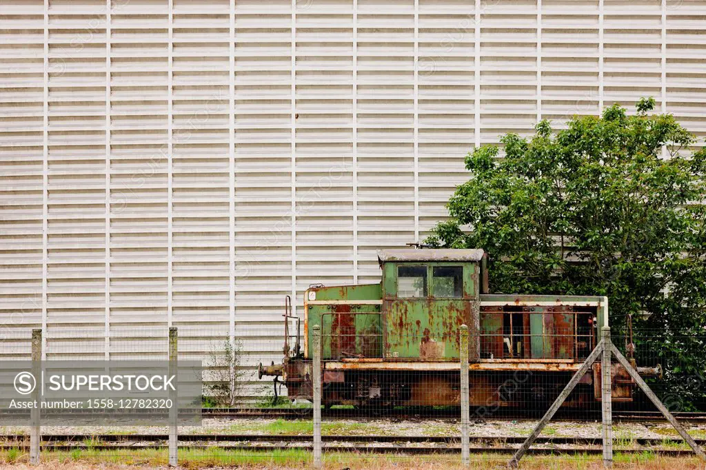 Discarded locomotive in front of industrial facade