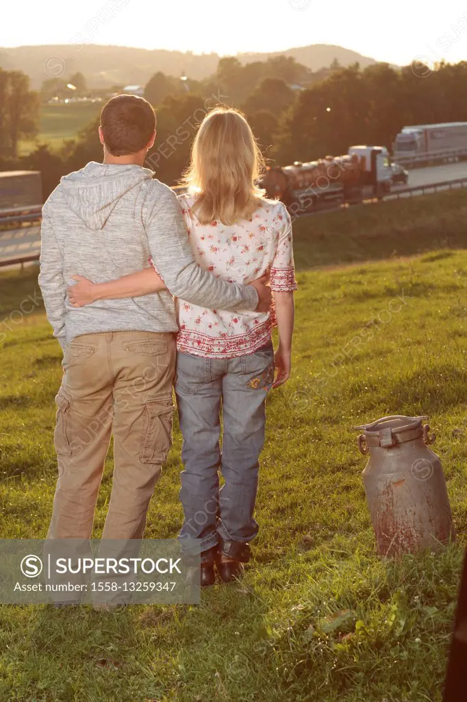 Couple, young, meadow, standing, arm in arm, back view, milk churn,