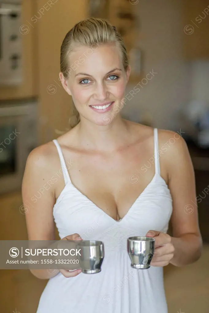 Young woman in the white dress is holding two cups of espresso in the kitchen
