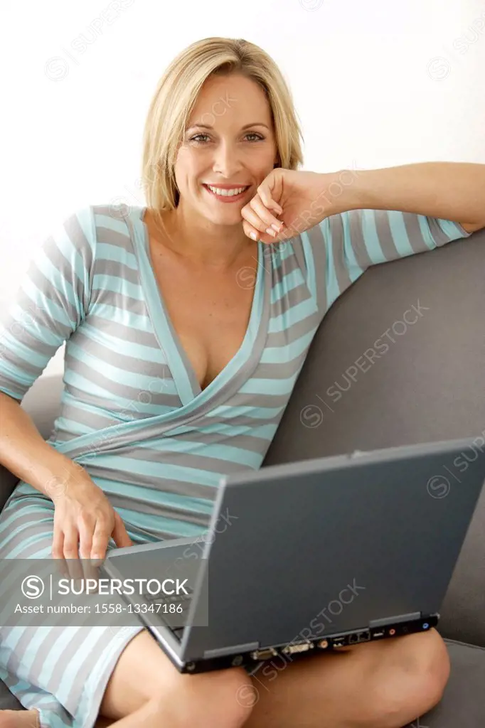 Young smiling woman is sitting with laptop on sofa