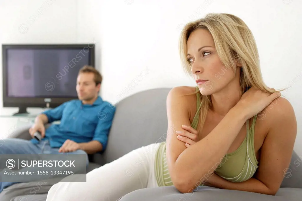 Couple is sitting on sofa with television in the background, she is upset in the foreground