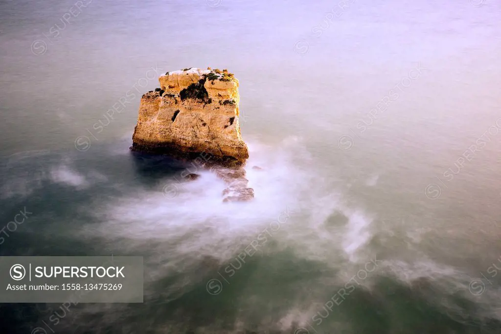 A single rock in the surf in the evening light